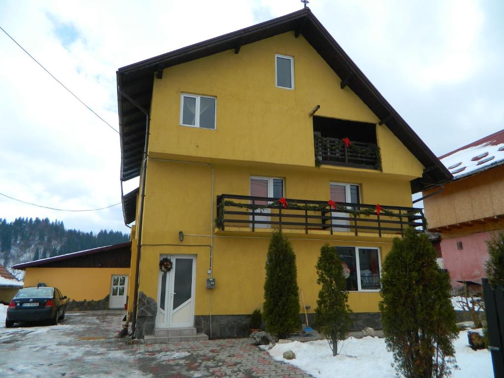 a yellow house with a balcony with red flowers on it at Pensiunea Buzdugan in Moieciu de Jos