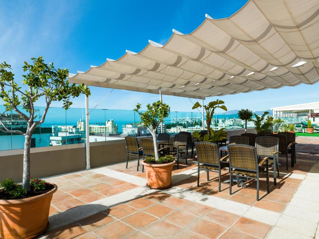 een patio met tafels en stoelen onder een witte parasol bij Hotel Monarque El Rodeo in Marbella