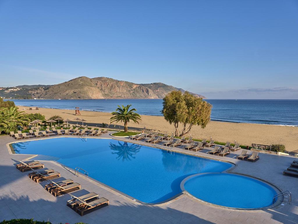 a large swimming pool with chairs and a beach at Pilot Beach Resort in Georgioupolis