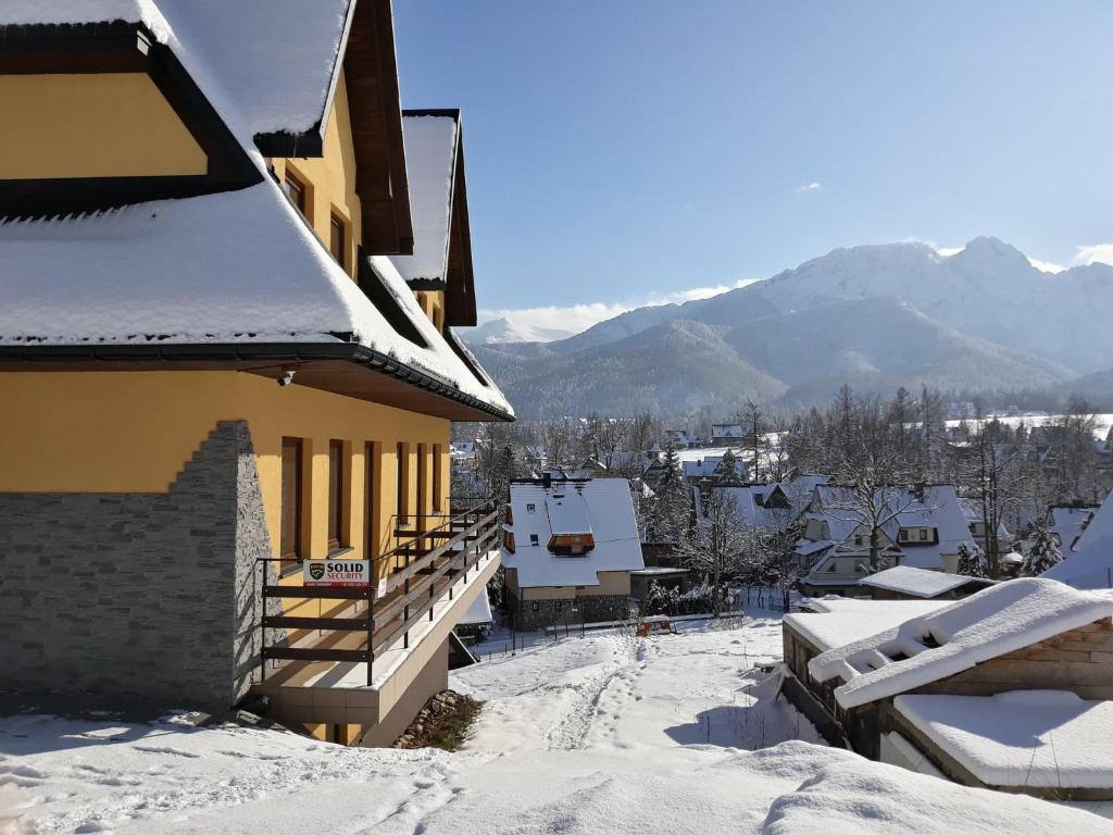 a building covered in snow with mountains in the background at Pokoje przy Szymoszkowej in Zakopane