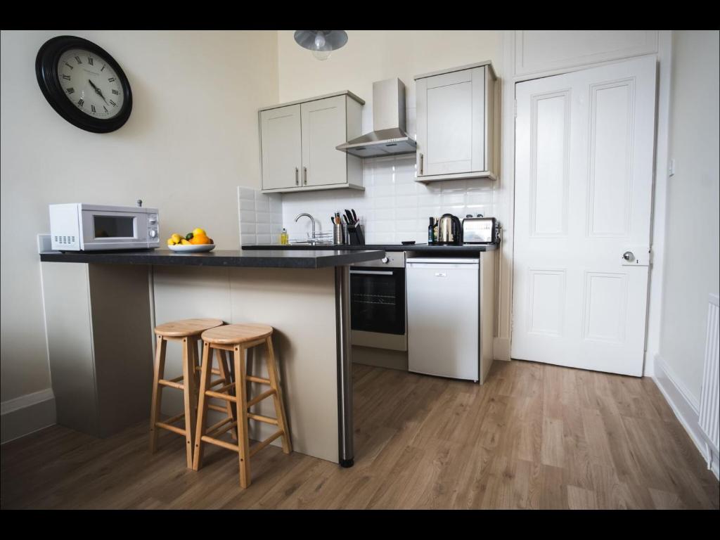 a kitchen with a counter and stools and a clock on the wall at Cedar Apartment in Helensburgh