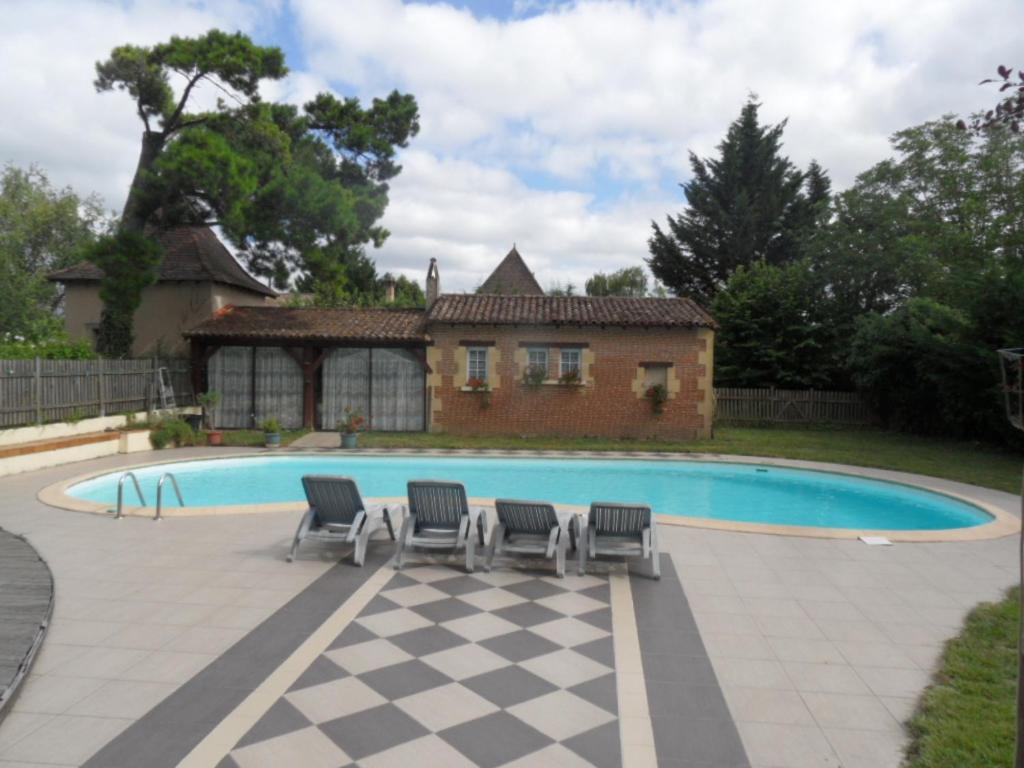 uma piscina com quatro cadeiras e uma casa em B&B La Viderente em Saussignac