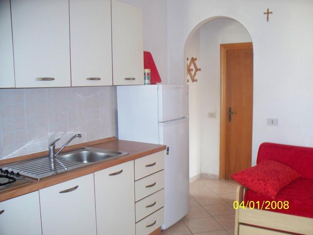 a kitchen with white cabinets and a sink and a red chair at Appartamenti Helvetia in Peschici