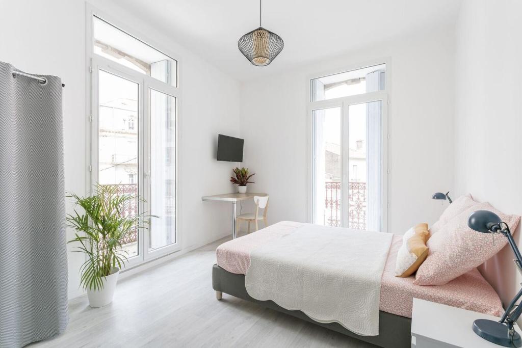 a white bedroom with a bed and two windows at Sunny Relaxing Apartement in Béziers