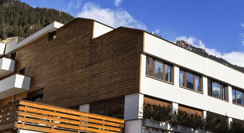 un edificio marrone e bianco con una montagna sullo sfondo di Hotel Club Regina E Fassa a Mazzin