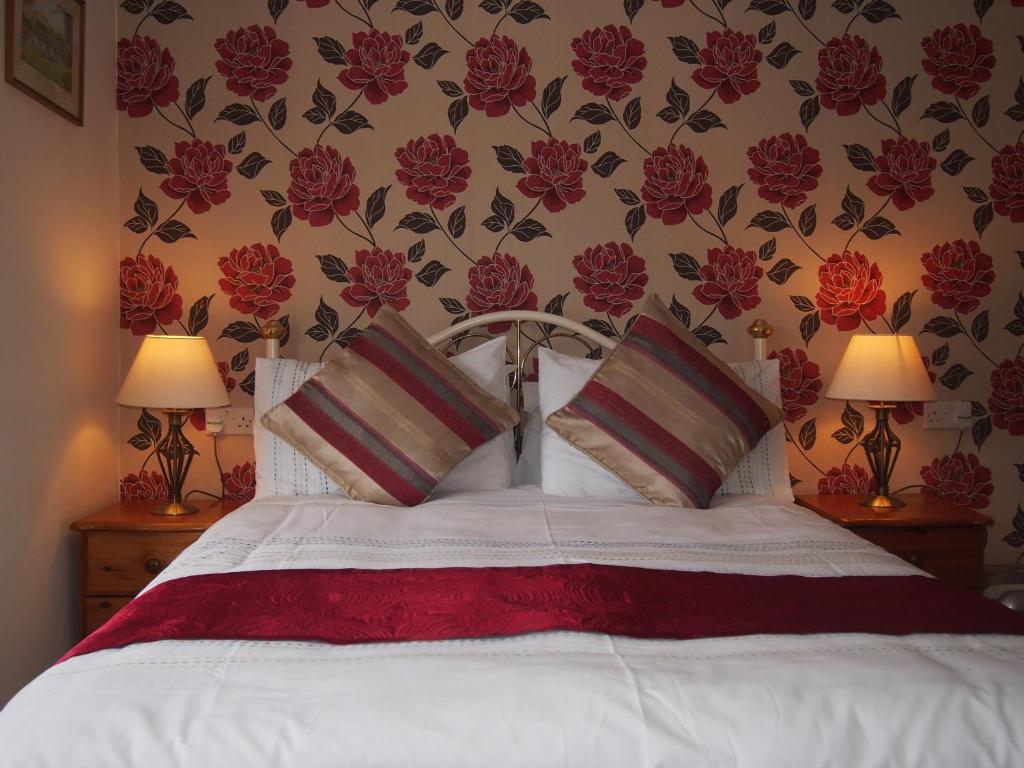 1 dormitorio con 1 cama con flores rojas en la pared en Bodhyfryd Guesthouse en Betws-y-coed