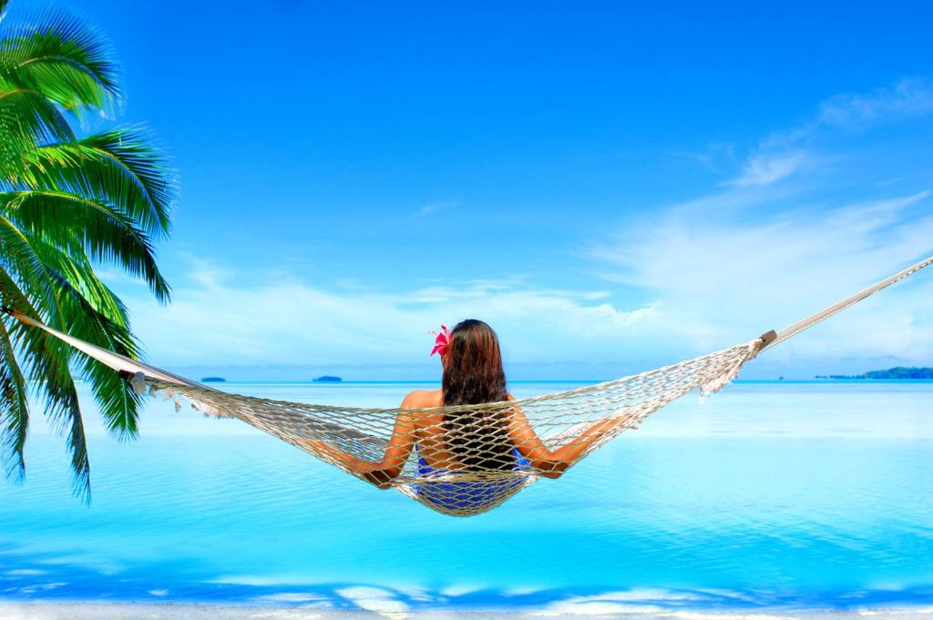 a woman sitting in a hammock on a beach at Aitutaki Lagoon Private Island Resort (Adults Only) in Arutanga