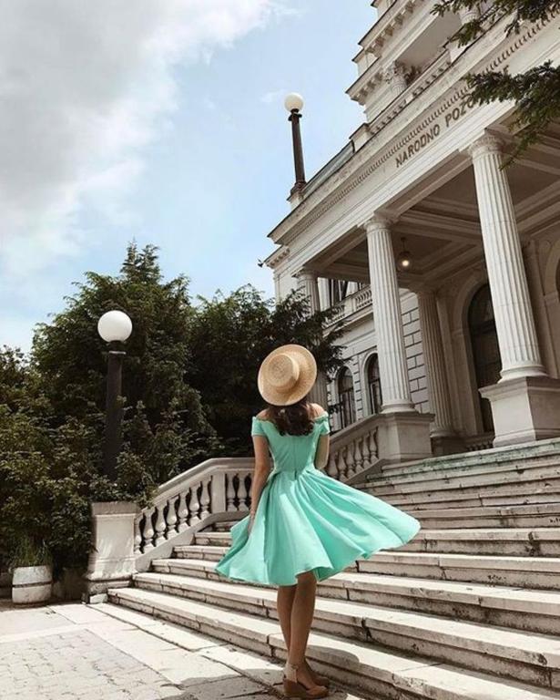 a woman in a blue dress and a hat standing on some stairs at Apartment Milk&Honey - free Parking in Sarajevo
