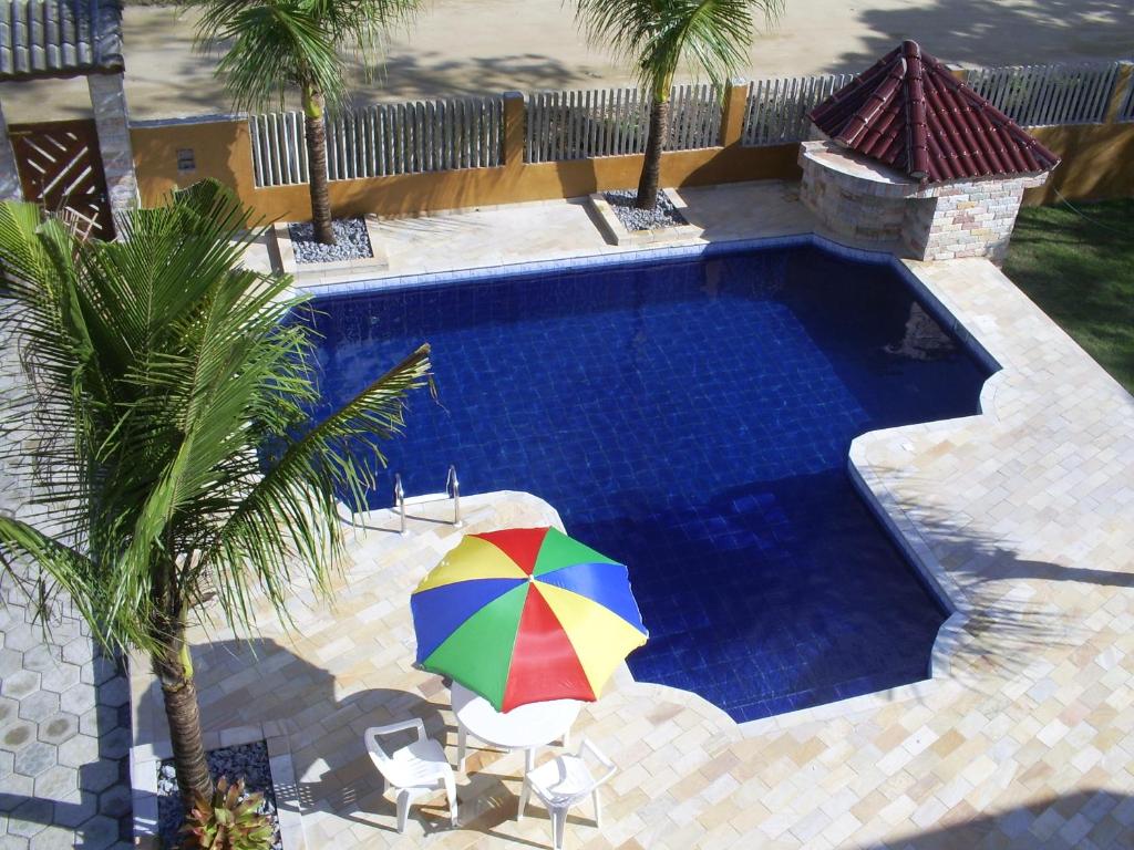 an umbrella next to a swimming pool with palm trees at Kitnets Park Verde in Peruíbe