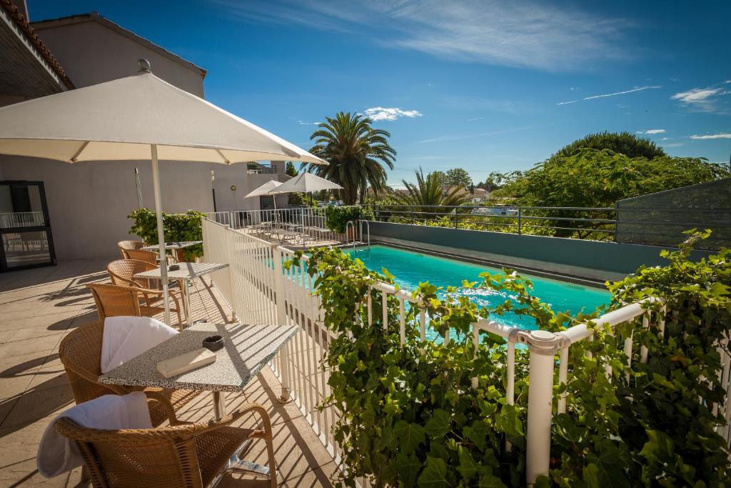 a swimming pool with tables and chairs and an umbrella at Hotel Canal Aigues Mortes in Aigues-Mortes