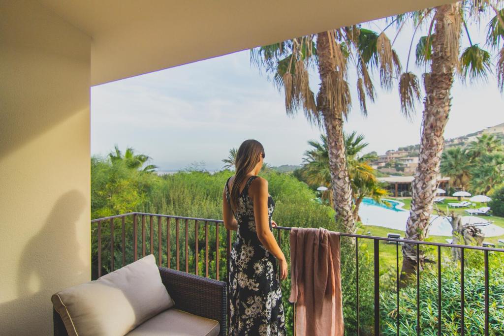 a woman standing on a balcony looking out at the palm trees at Hotel Aquadulci in Chia