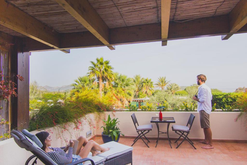 a man standing on a patio with two women laying on chairs at Hotel Aquadulci in Chia