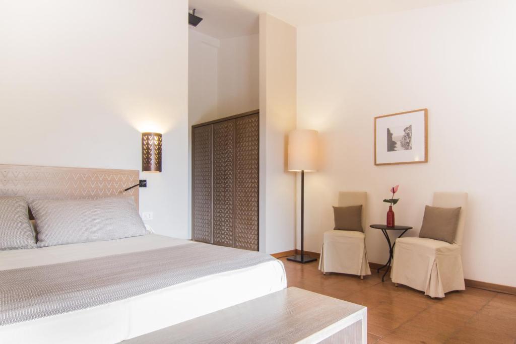 a white bedroom with a bed and two chairs at Hotel Aquadulci in Chia