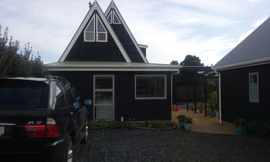 a black house with a pointed roof with a car parked in front at Near the shore in Waikanae