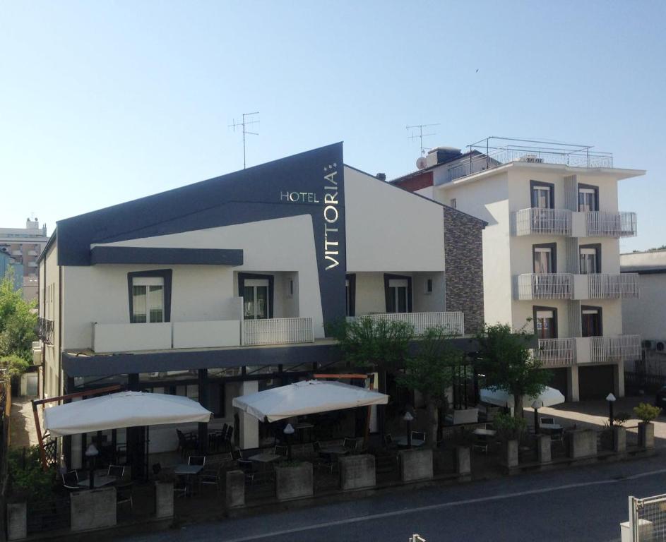 un hotel con mesas y sombrillas frente a un edificio en Hotel Vittoria en Gatteo a Mare