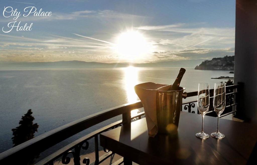 Balcony with ice bucket of champagne and two wine glasses overlooking the bay and sunlit coastline; 'City Palace Hotel' logo at City Palace Hotel in Ohrid