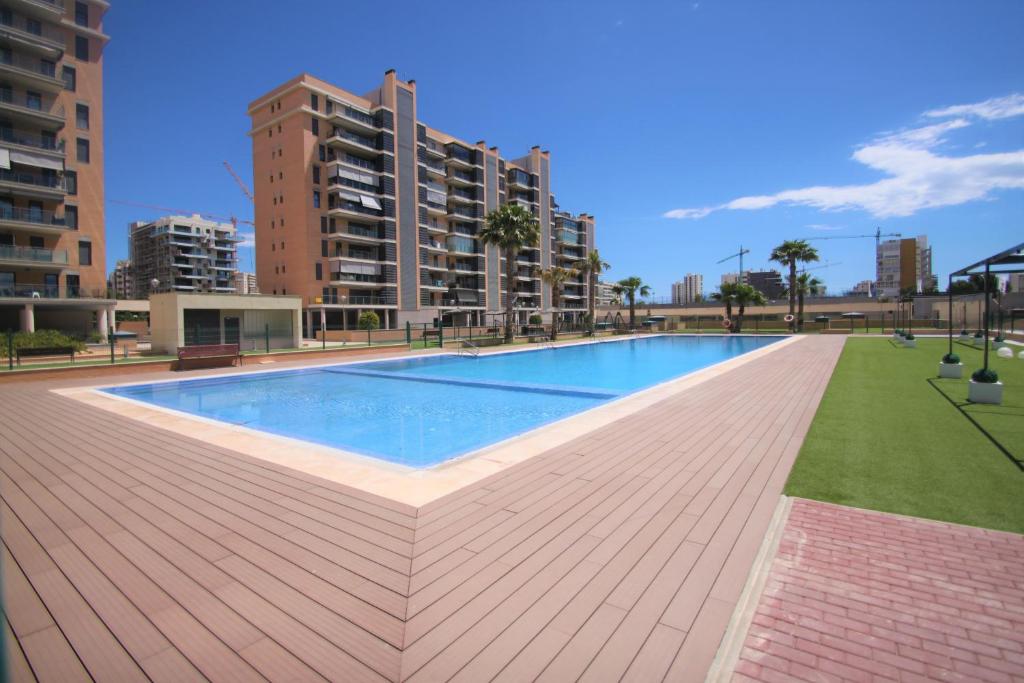 een groot zwembad op een houten terras met gebouwen bij CasaTuris Playa, piscina y parking en Residencial San Juan SJ102 in Alicante