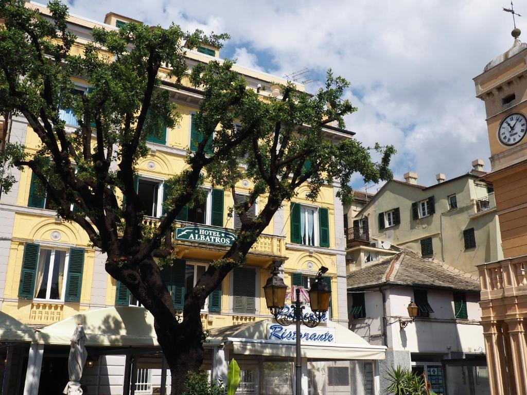 a tree in front of a building with a clock tower at hotel albatros in Arenzano