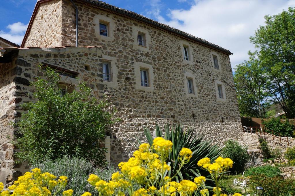 um antigo edifício de pedra com flores amarelas no primeiro plano em Gîte **** "le refuge des fées" em Saint-Julien-du-Gua