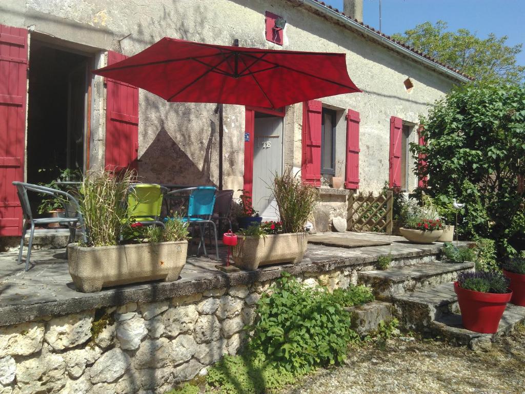 a patio with a red umbrella and chairs and a house at Le champ des étoiles in Massoulès
