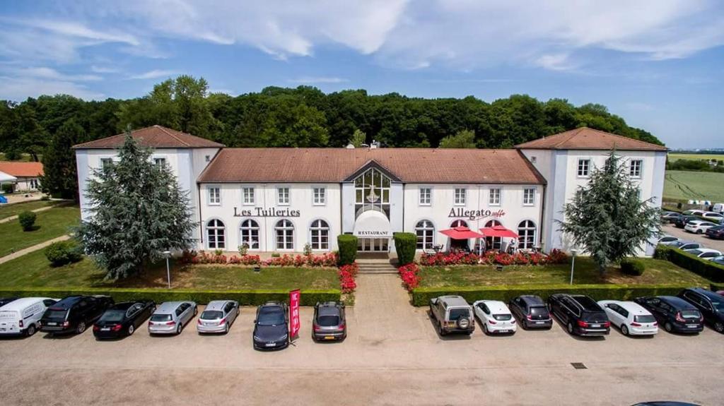 un grande edificio bianco con auto parcheggiate in un parcheggio di Logis Hôtel Les Tuileries a Féy