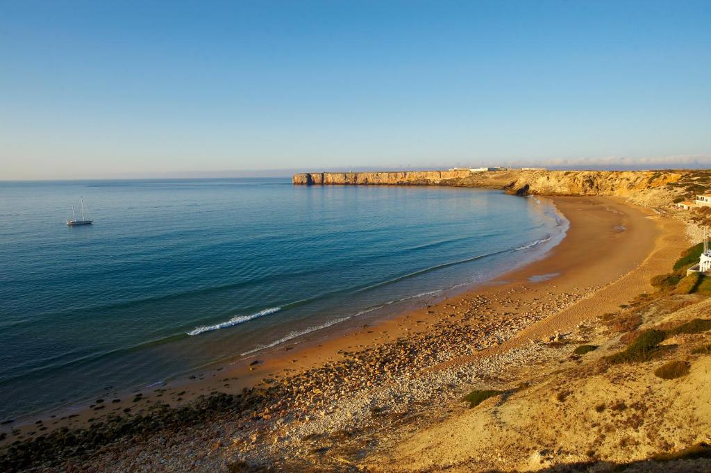 a view of a beach with a boat in the water at Martinhal Sagres Beach Family Resort Hotel in Sagres