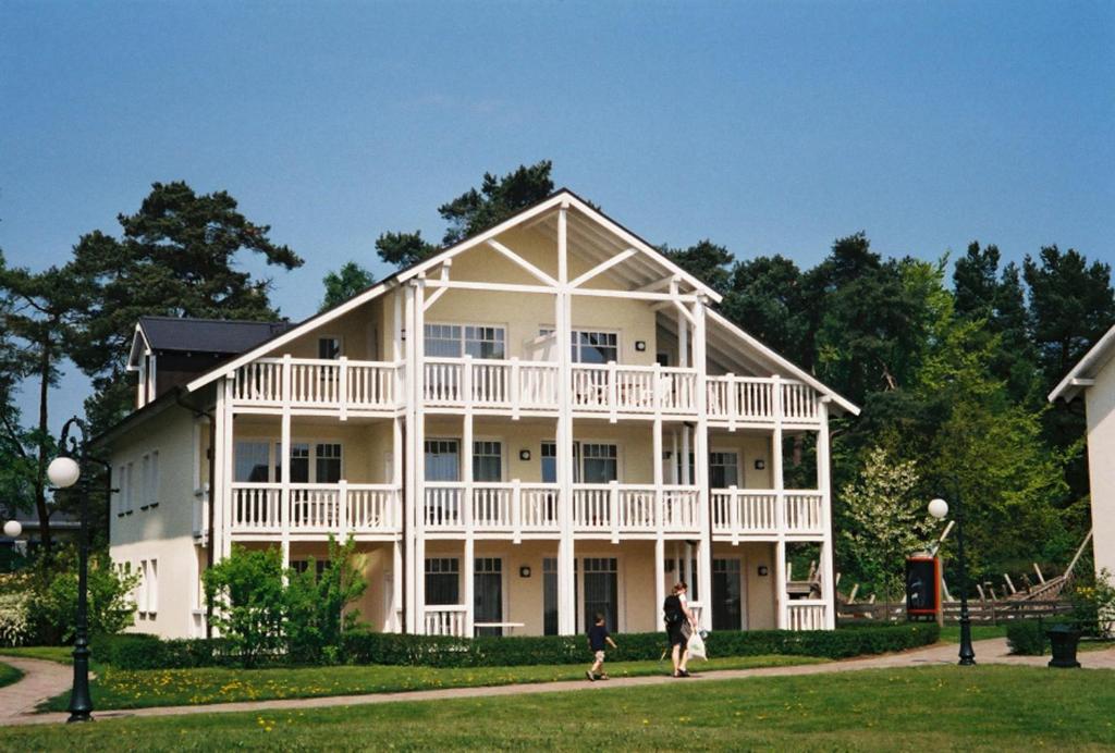 ein großes weißes Haus mit zwei Leuten, die davor laufen in der Unterkunft Dünenpark Binz by Rujana in Binz