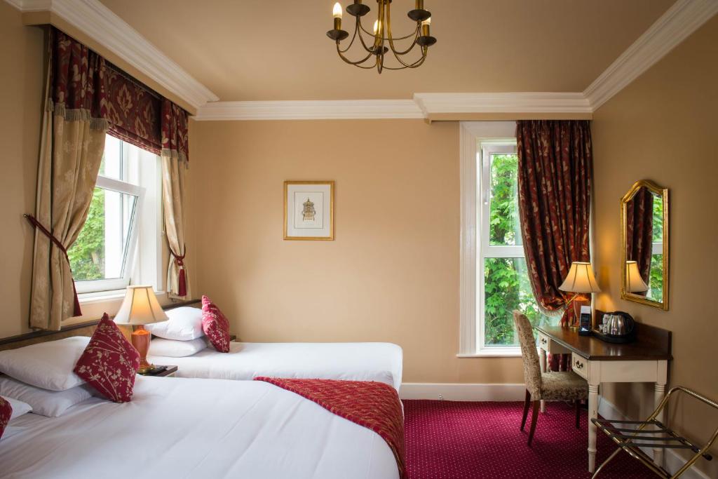 a hotel room with two beds and a desk and two windows at Gabriel House Guesthouse in Cork