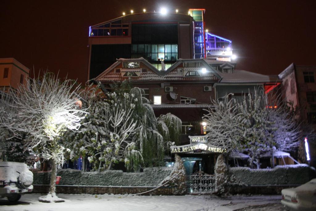 budynek z pokrytymi śniegiem drzewami przed nim w obiekcie Hotel Bar Restaurant America w mieście Kukës
