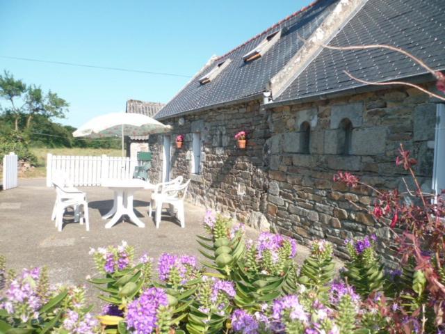 - un bâtiment en pierre avec une table, des chaises et des fleurs dans l'établissement P'ty gîte de Bréharadec, à Goulien