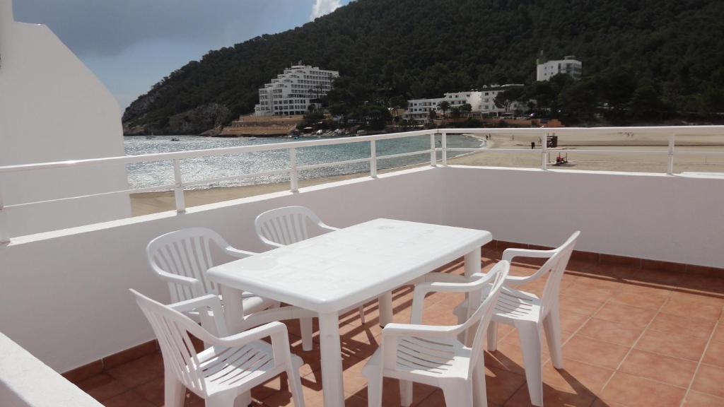 een witte tafel en stoelen op een balkon met uitzicht op de oceaan bij Apartamentos Cala Llonga in Cala Llonga