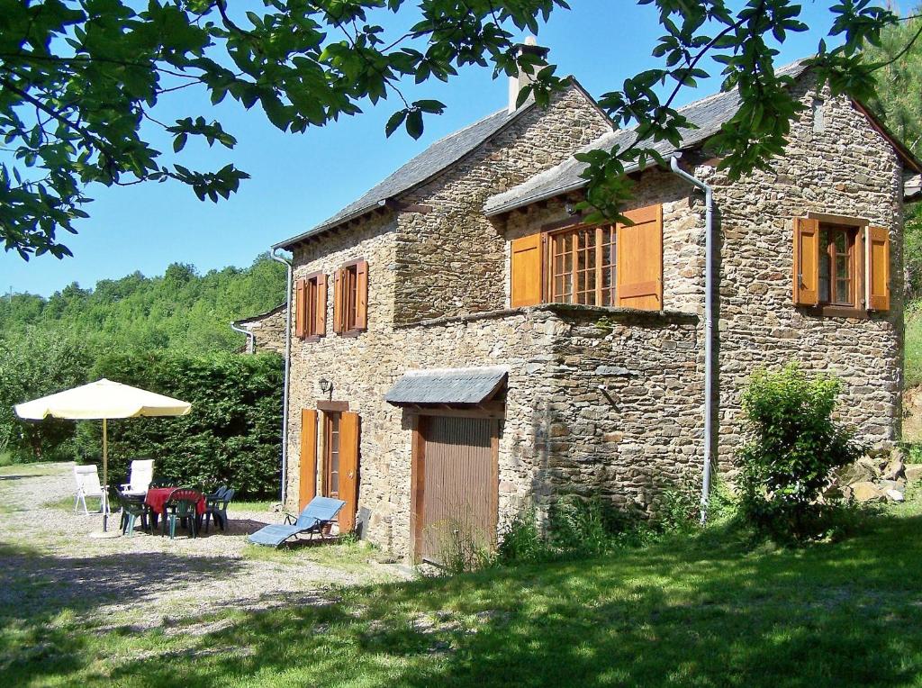 una antigua casa de piedra con una mesa y una sombrilla en Les gîtes du Mas Brunet en Cadix