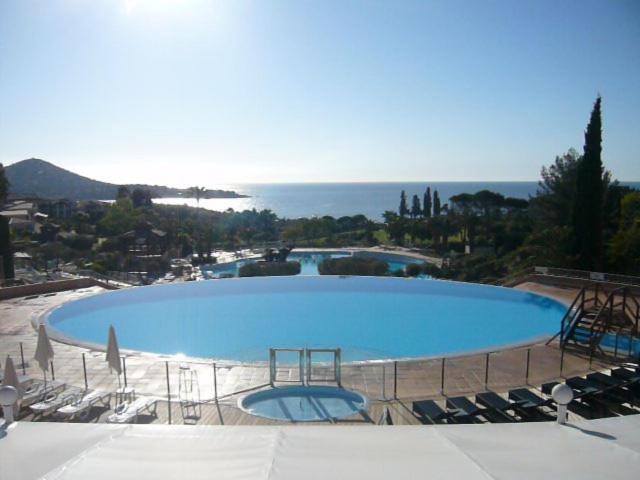 une grande piscine bleue avec des chaises et l'océan dans l'établissement Cap Esterel place des pecheurs, à Agay