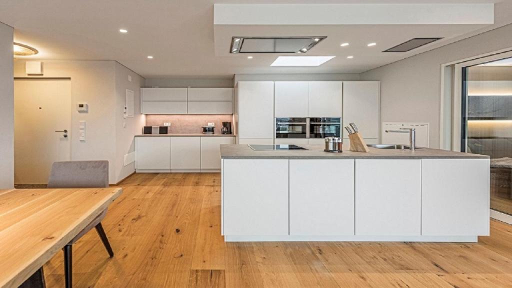uma cozinha em plano aberto com armários brancos e uma mesa de madeira em Penthouse Skygarden em Scena