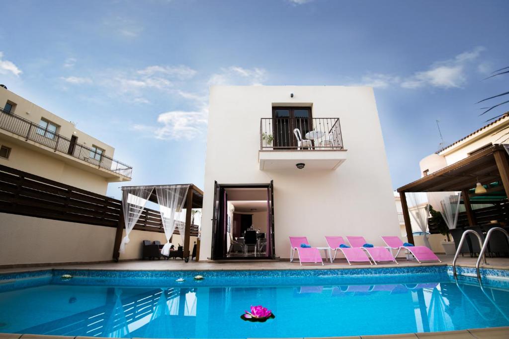a swimming pool with pink chairs and a building at Luxury Villa Regina in Protaras