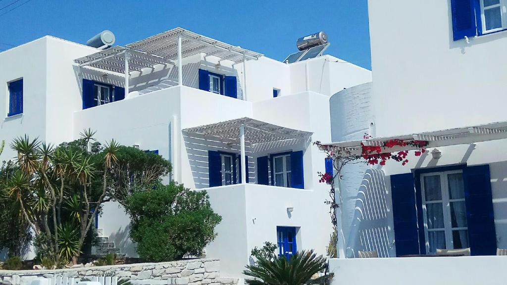 a white building with blue windows and palm trees at Nicos Studios & Apartments in Logaras