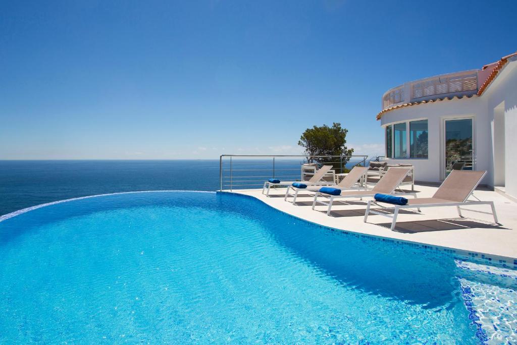 a swimming pool with chairs and the ocean in the background at Blue Dream Villa in Jávea
