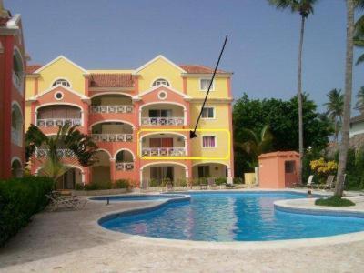 un grand bâtiment jaune et rose avec une piscine dans l'établissement Apartamento B6 El Dorado en Bávaro - Punta Cana, à Punta Cana