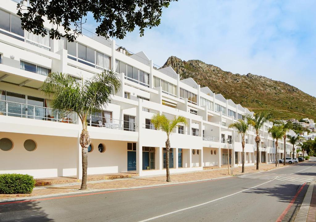 a white building with palm trees in front of it at First Group Cape Gordonia in Gordonʼs Bay