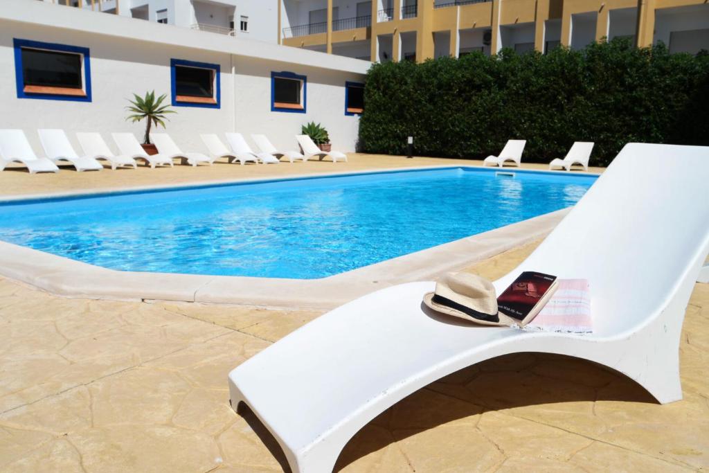 a white lounge chair with a hat sitting next to a swimming pool at Via Dona Ana in Lagos