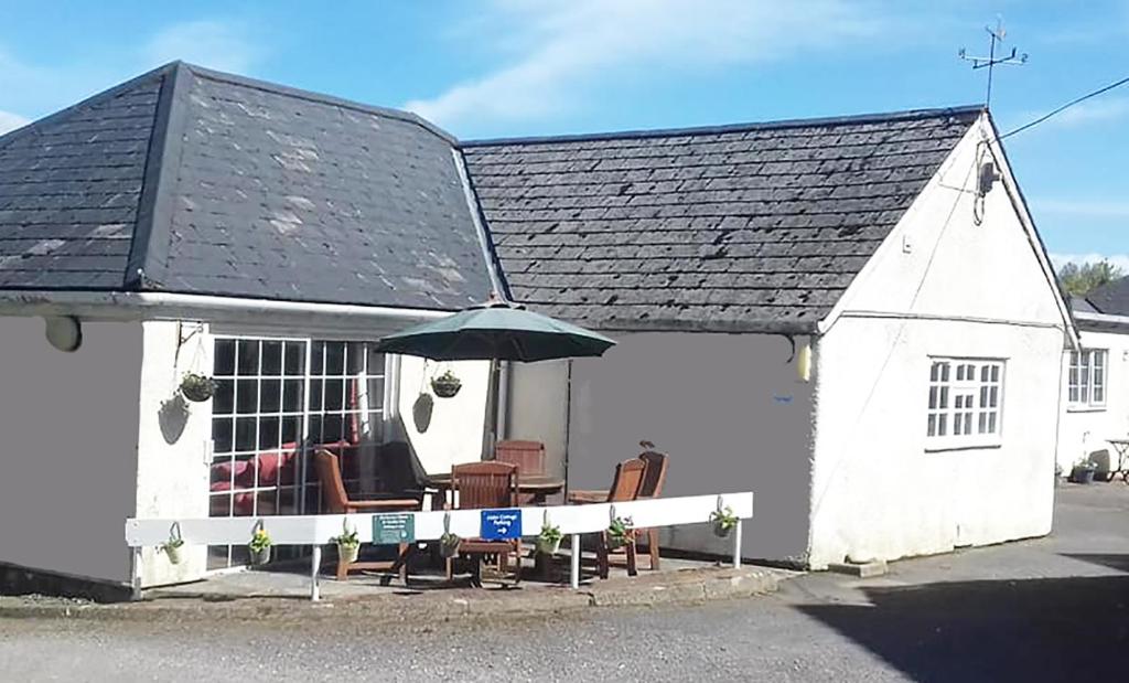 un pequeño edificio blanco con sillas y sombrilla en Alder Cottage, en Tiverton