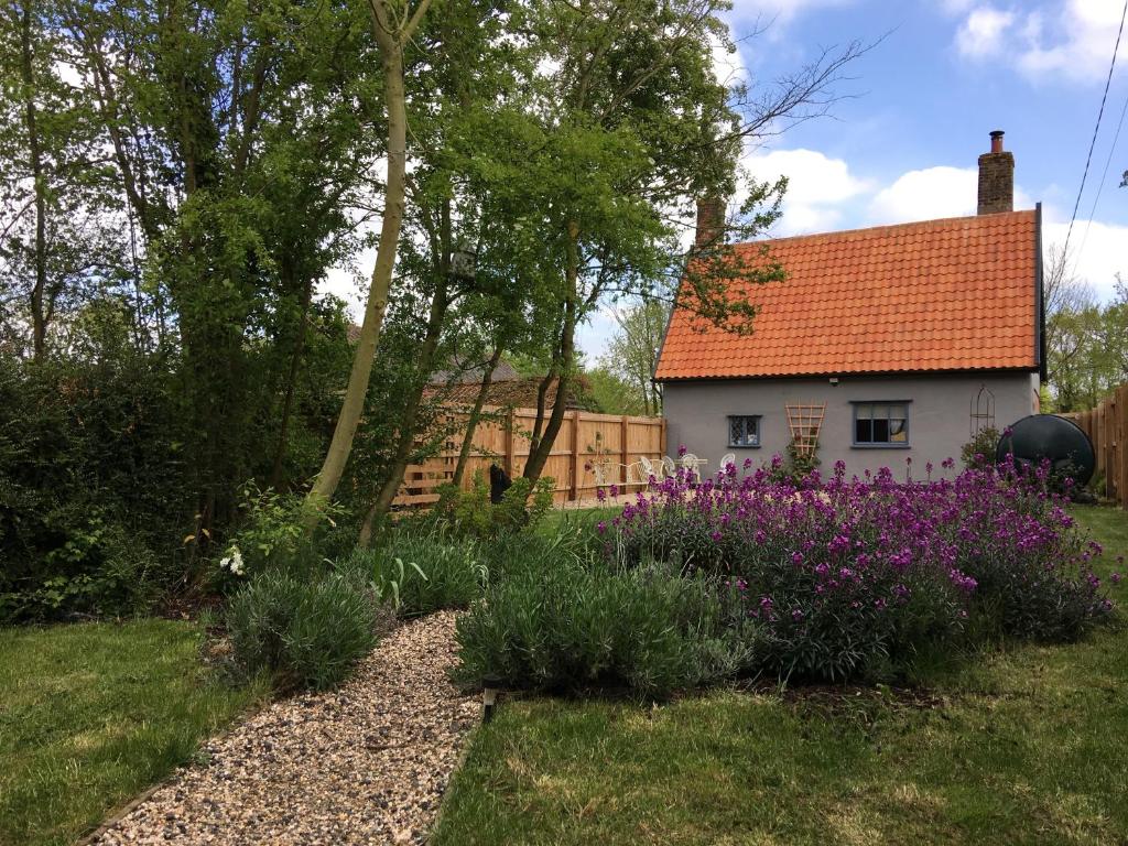 een wit huis met een rood dak en paarse bloemen bij Watt Cottage in Ipswich