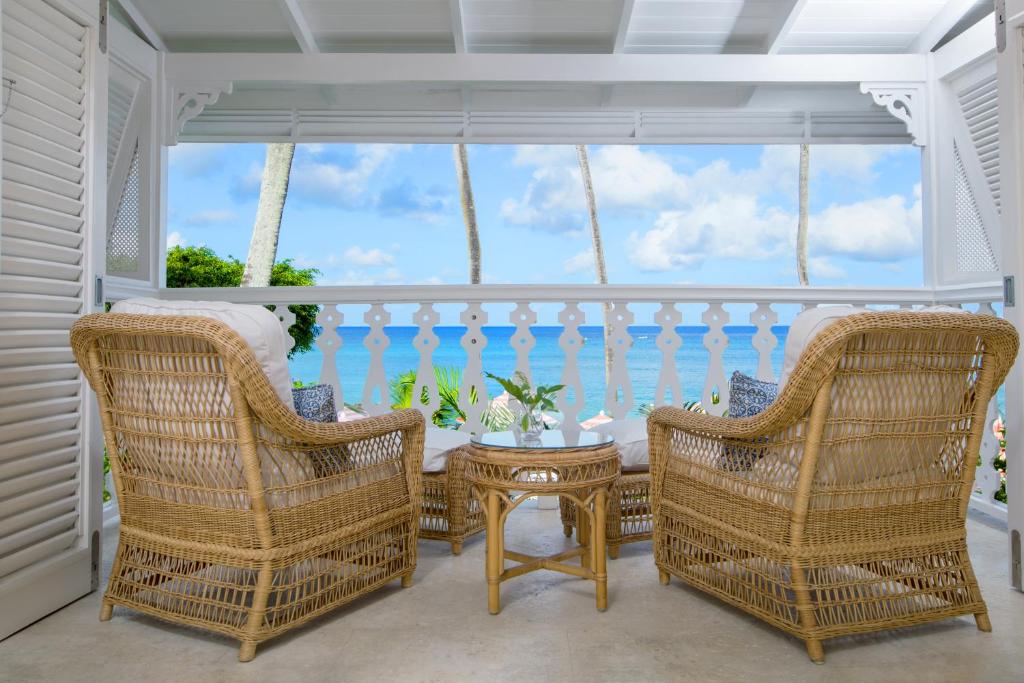 a porch with wicker chairs and a table and the ocean at Cobblers Cove - Barbados in Saint Peter