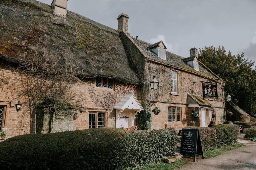 un antiguo edificio de piedra con techo de paja en The Falkland Arms, en Chipping Norton