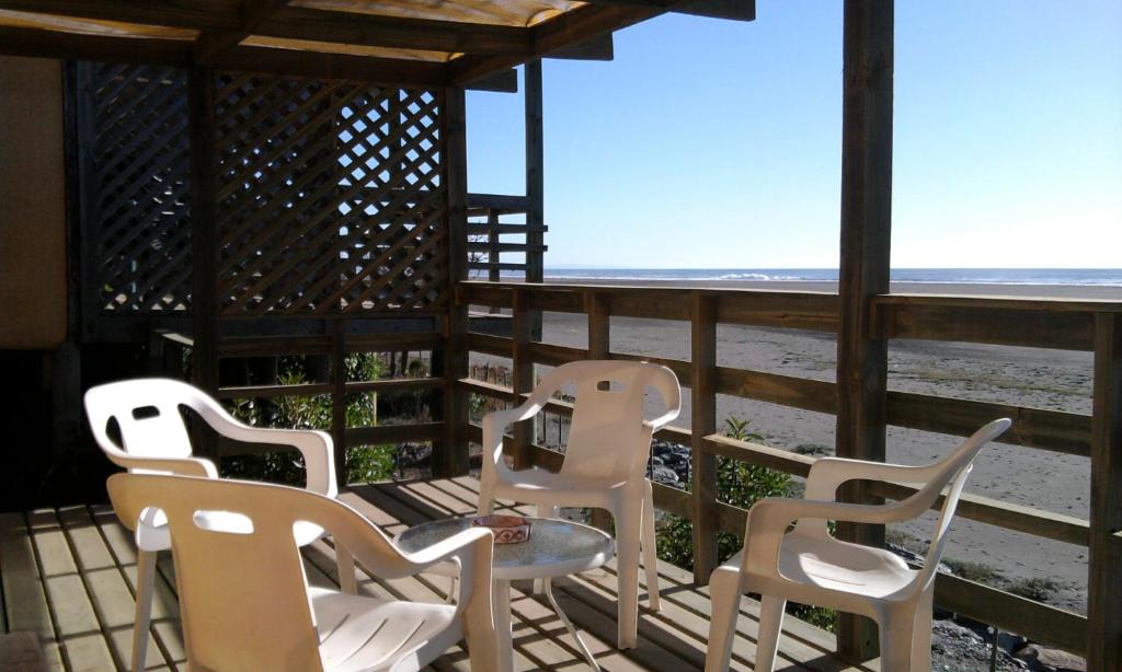drie stoelen en een tafel op een veranda met het strand bij Cabañas del Rio - La Pesca - Region del Maule in Iloca