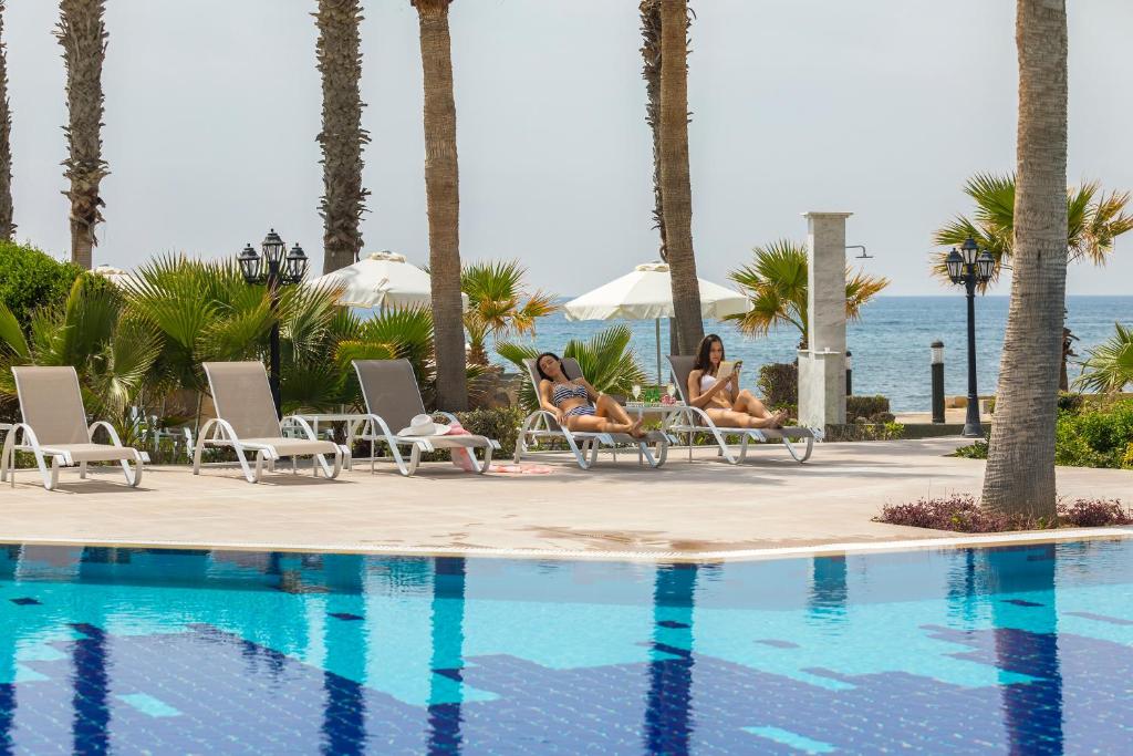 two women sitting in chairs next to a swimming pool at Aquamare Beach Hotel & Spa in Paphos