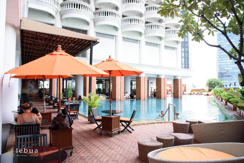 A pool terrace with orange umbrellas, shaded seating, and the hotel’s curved facade.