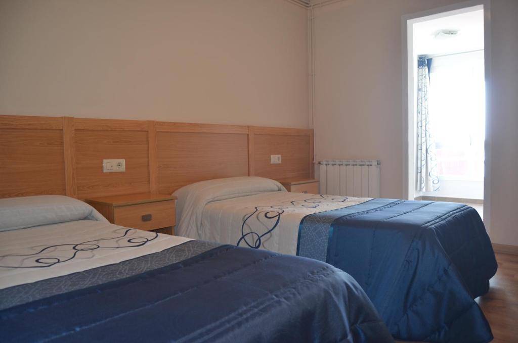 Habitación con 2 camas con sábanas azules y ventana en Del Peregrino, en Arzúa