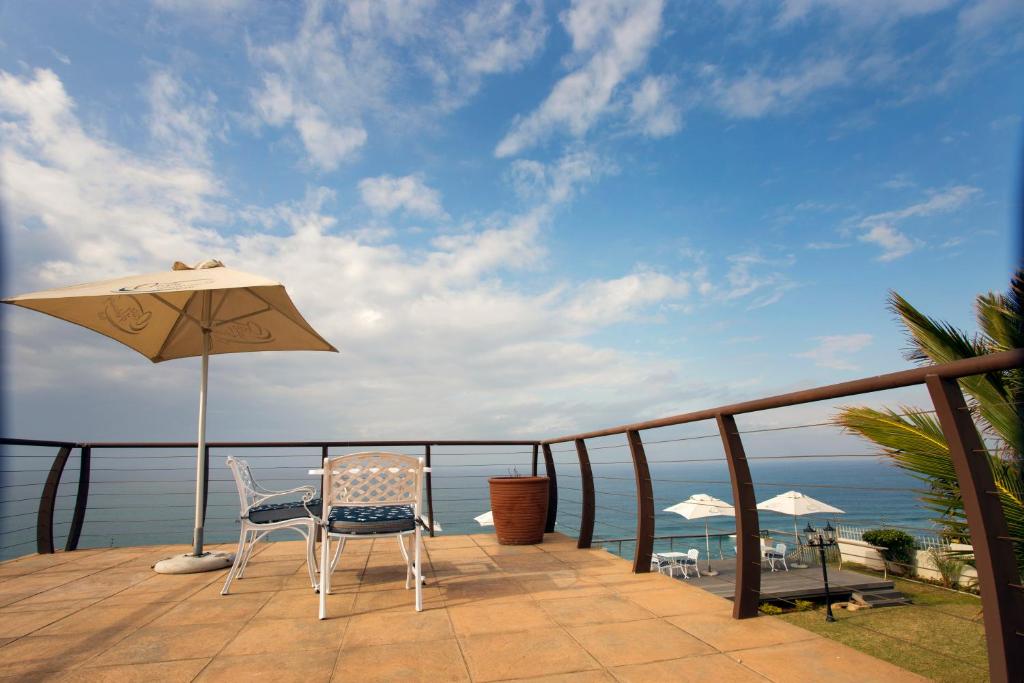 a balcony with a table and an umbrella and the ocean at Ocean Hideaway Bed and Breakfast in Amanzimtoti