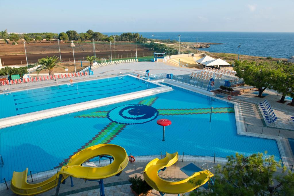 une grande piscine avec des toboggans jaunes et l'océan dans l'établissement Corvino Resort, à Monopoli